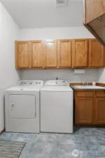 Functional laundry room with utility sink, storage cabinetry, and space for full-size washer and dryer.