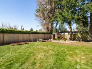 Expansive fully fenced backyard with fire pit and garden beds.