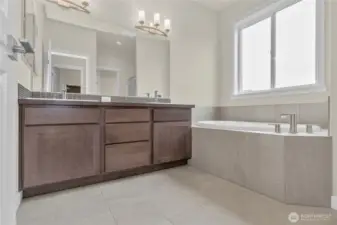 Primary bathroom has a double vanity with undermount dual sinks, tile floor, quartz countertops and a soaking tub with tile surround.