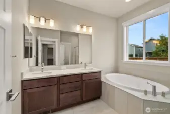Primary bathroom has a double vanity with undermount dual sinks, tile floor, quartz countertops and a soaking tub with tile surround.