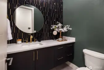 Bold and sophisticated, the main floor powder room features a dramatic tiled accent wall, brass fixtures, and sleek modern cabinetry