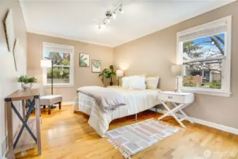 Bright windows on two walls fill this main-floor bedroom with natural light, complemented by hardwood floors and classic crown molding.
