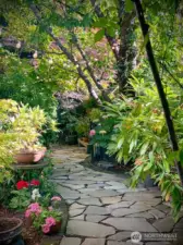 Meander along flagstone paths through lush seasonal landscaping, creating a peaceful backyard escape filled with color and texture. Photo provided by owner to illustrate seasonal landscaping as it matures and blooms.