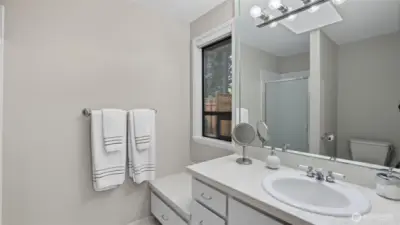This private ensuite offers spacious counterspace, built-in storage, and a frosted glass shower.