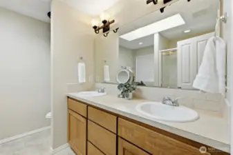 Tall vanity and double sinks with tile backsplash are enhanced by the full-width mirror and skylight.