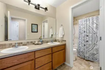 Hall bath with dual vanity and tile backsplash; smart separated design allows for easy sharing. Full tub/shower combo seen ahead.