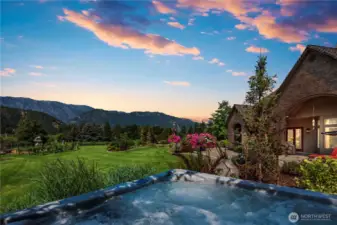 Beautiful outdoor living space featuring a hot tub, manicured grounds, and breathtaking sunset views across the valley toward the Cascade Mountains and Enchantment Range.