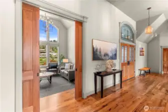 Beautifully detailed hallway with hardwood flooring and sliding doors that reveal a bright sitting room framed by a striking arched window.