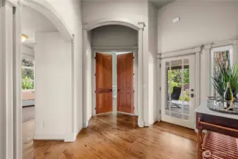 Refined hallway featuring classic archways, rich hardwood floors, and elegant double doors that lead into the private primary suite.