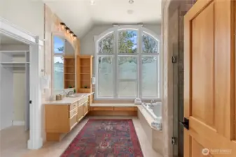 Elegant primary bath retreat featuring custom cabinetry, expansive vanity space, and a dramatic arched window that fills the room with natural light, complemented by a soaking tub and spacious walk-in closet.