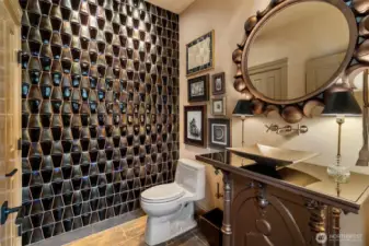 The powder room makes a statement with a hand-made glass tile wall and a bronze Zen sink by Stone Forest, creating a unique and elevated space.