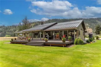 A striking single-level home with a sleek metal roof and expansive deck designed for outdoor living. Surrounded by vibrant green lawn and mountain views, this residence offers the perfect balance of modern elegance and natural tranquility.
