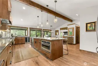 The large central island with waterfall edges becomes the focal point, offering seating for four and ample prep space under elegant pendant lighting.