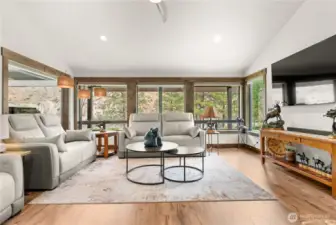 A wall of expansive windows fills this cozy living space with natural light while framing serene views of the surrounding landscape. Neutral tones, elegant wood accents, and contemporary furnishings make this room a stylish yet welcoming retreat.