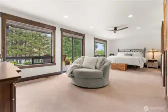 This spacious primary bedroom offers a serene retreat with expansive windows that frame picturesque views of the surrounding trees and landscape. The room is filled with natural light, and features a cozy reading nook with a plush round swivel chair, perfect for relaxing. Sliding glass doors provide direct access to a private outdoor patio area, seamlessly blending indoor comfort with outdoor tranquility.