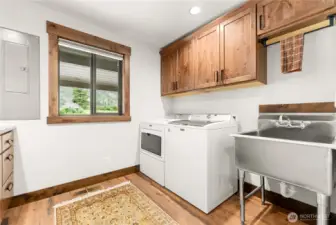 Bright and functional laundry room featuring modern Maytag washer and dryer, stainless steel utility sink, and abundant cabinetry for organization. Large window brings in natural light and frames peaceful mountain views, making everyday chores more enjoyable.