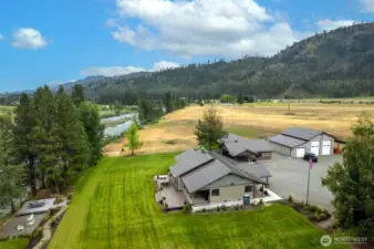 From above, the property reveals its perfect blend of comfort and function: a beautiful craftsman-style home with expansive decking, a large shop/garage for all your needs, and a sprawling lawn bordered by riverfront access and natural beauty.