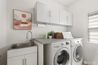 The large laundry room/mudroom located just off the kitchen and adjacent to the attached garage features utility sink, folding table, coat/backpack hooks and ample cabinetry.