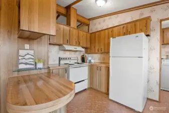 Looking across the eating bar toward the range and refrigerator side of the kitchen. There are a lot of cabinets for storage as well as a pantry in the laundry room beyond.