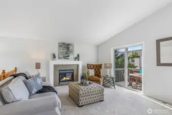 The living room is highlighted by vaulted ceilings and a gas fireplace—an inviting focal point for everyday comfort. A large sliding door opens to the deck for effortless indoor-outdoor flow, complemented by new carpet and a calming, neutral palette.