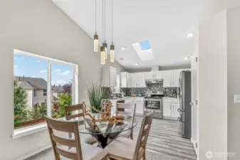The dining area sits by an expansive window with treetop outlooks, accented by modern pendant lighting. New luxury vinyl plank extends from here into the kitchen, while the open sightlines keep everyone connected.