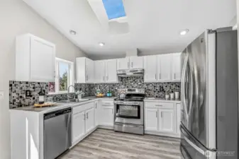 Crisp white cabinetry, mosaic tile backsplash, and stainless appliances define the kitchen. A skylight and window over the sink bathe the workspaces in natural light, while new LVP flooring offers durability and style.