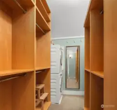 A very large walk-in closet with extensive built in cabinetry includes a stack Miele washer/dryer and custom closet hanging and folding cabinetry.