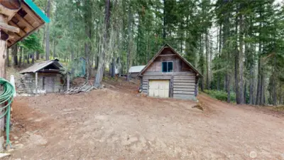 Detached log garage with upper space, plus rustic stone outbuilding nestled among the trees.