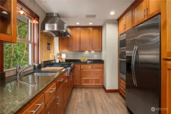 An abundance of cherry wood cabinets (some with glass doors) and natural stone counters complimented by tile backsplash and wood flooring.