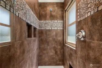 Custom tiled shower with 2 product niches and decorative band accented by natural light.