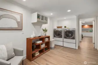 This basement laundry area features side-by-side front-loading washer and dryer units, known for their energy efficiency and gentle handling of clothes. The side-by-side arrangement offers convenient access to both machines, making laundry tasks more manageable. Plenty of shelf space for detergents, a hanging rack, and room for a large table for folding.