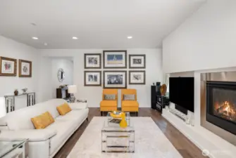 Open living room features sleek fireplace, wide-planked flooring, mirroring windows and recessing lighting.