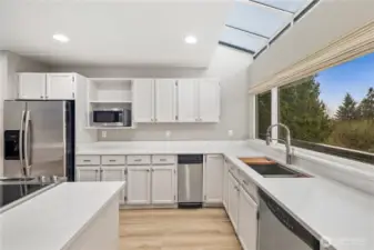 Bright modern kitchen with white cabinetry, quartz counters, skylight, stainless appliances, expansive window, and clean lines designed for effortless entertaining.
