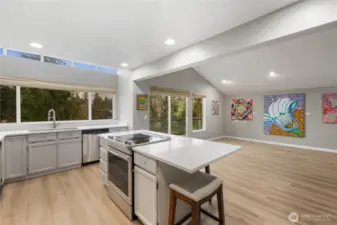 Bright open kitchen and living space with oversized island, seating, expansive windows, wide plank floors, and gallery-worthy wall art displays.