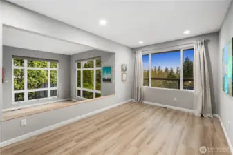 Light-filled living and dining space features wide windows, gray freshly painted tones, recessed lighting, and warm wood floors opening to tranquil views.