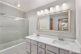 Sleek lower level updated bathroom featuring double vanity, quartz counters, framed mirror, modern lighting, glass shower enclosure, and clean contemporary finishes.