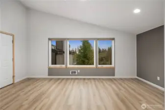 Bright bedroom featuring wide plank floors, large windows overlooking greenery, neutral tones, recessed lighting, and peaceful, airy atmosphere.