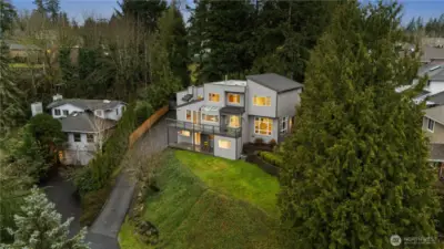 Elevated modern home nestled among evergreens, offering privacy, terraced landscaping, hillside setting, and glowing interiors framed by serene natural surroundings. Easterly views of  Cascade mountains year round.