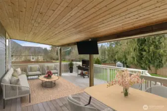 From this angle, the covered deck feels like a true extension of the home. The wood plank ceiling with two storage compartment access brings in that cozy, finished feel, while the white bannisters keep it bright and classic. There’s plenty of space for a dining table, seating, and a barbecue setup, and the mounted TV stays with the home for effortless outdoor entertaining. It’s a great vantage point over the backyard and one of those spaces you’ll use way more than you expect.