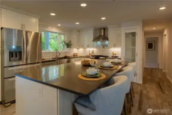 Quartz countertop, stainless steel appliances, mounted pot filler over gas range. Oversize island has storage cabinets on both sides.