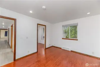 Another view of the primary bedroom showcasing its bright window, recessed lighting, and rich flooring. This angle highlights the functional layout with direct access to a secondary bedroom or office space, offering flexibility for a home office, nursery, or private retreat. The hallway connection creates a natural flow into the rest of the home.