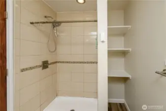 The walk-in tiled shower showcases a decorative mosaic accent strip and a rainfall-style showerhead. Built-in shelving provides convenient storage, while a frosted window brings in natural light while maintaining privacy. A comfortable and functional feature within the primary suite.