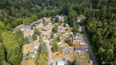 Expansive aerial perspective showcasing the property within its quiet neighborhood setting. Surrounded by mature evergreens and nearby homes, this location combines community living with a private, natural backdrop.