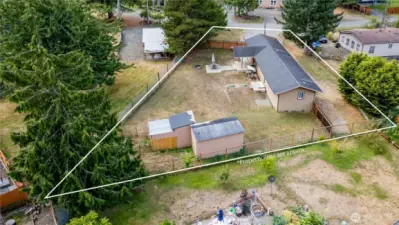 Aerial angle highlighting the backyard and outdoor living area. The property includes a patio, storage sheds, chicken coop and open yard space framed by fencing and trees, creating a versatile outdoor retreat.