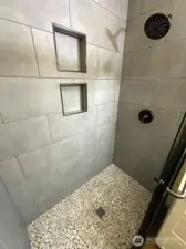 Remodeled Shower in primary suite has designer tile for mud pan and soap & shampoo niche