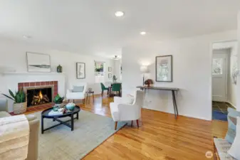 Bright open living room with wood burning fireplace, hardwood floors, and dining room towards the back.