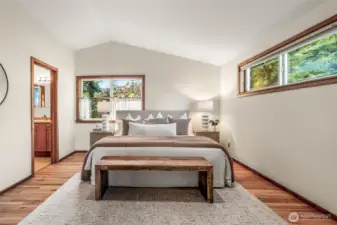 Large Primary Suite with vaulted ceilings and big windows feels spacious and airy. Full ensuite bathroom is on the left.