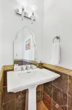 Main floor powder room with pedestal sink and travertine tiled walls.