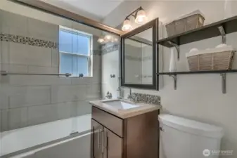 Full bathroom with tile accents and modern glass doors. Window to allow the light in.