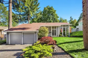 A beautifully maintained two-story home stands proudly, framed by mature landscaping and a manicured front lawn. The exterior showcases clean, timeless architecture with a charming covered porch, crisp trim details, and a tasteful blend of siding and stone accents.
